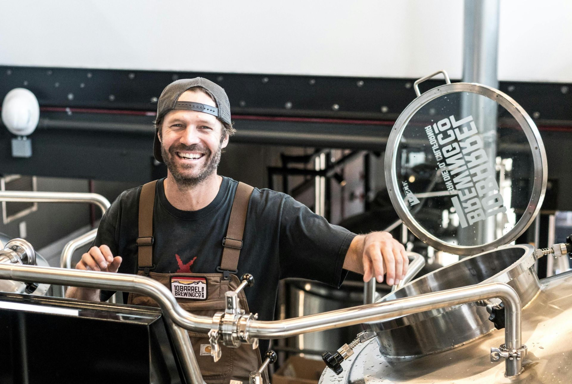 Happy brewer in a craft brewery standing near stainless steel equipment.