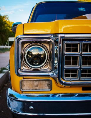 Close-up of a classic vintage yellow car's front grill and headlight showcasing its retro design.